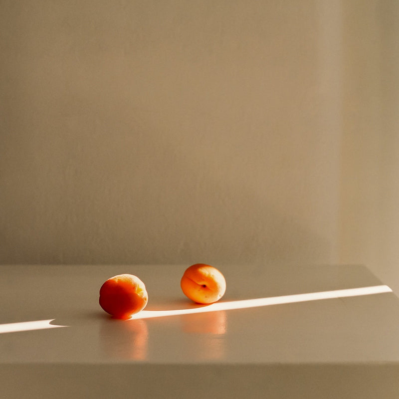 Two apricots on a reflective surface with a neutral background