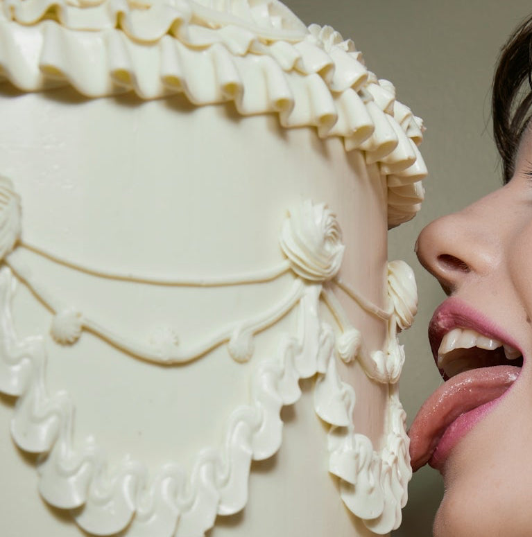 Close-up of a woman leaning in to bite into an intricately decorated cake.