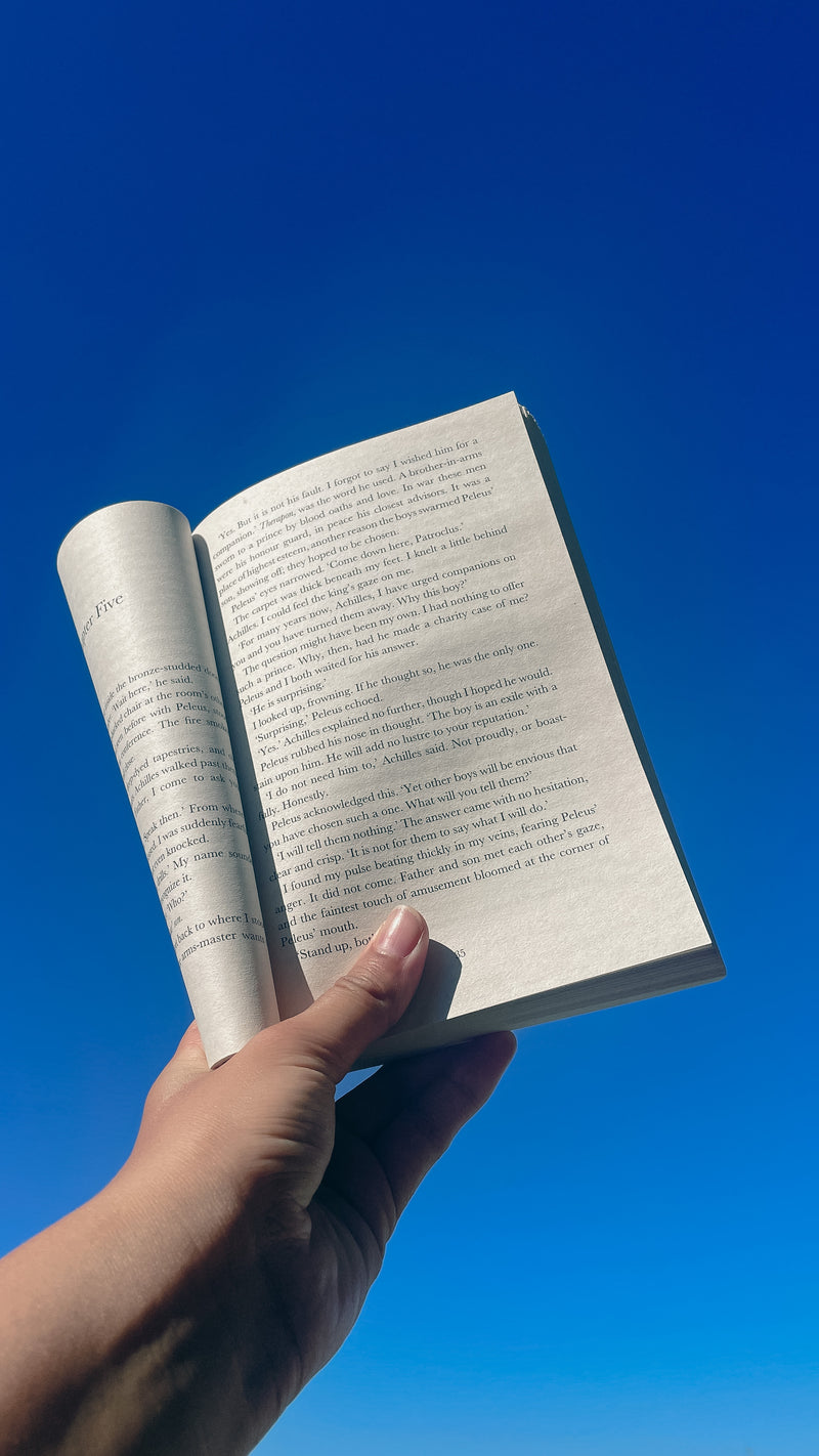 Hand holding an open book against a clear blue sky